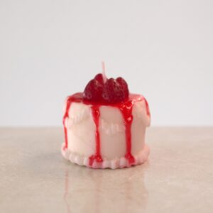 ela decorativa artesanal hiperrealista en forma de mini pastel con cobertura blanca, borde decorativo, sirope de fresa rojo goteando y fresas
