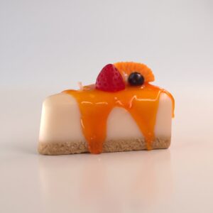 Vela decorativa artesanal hiperrealista en forma de porción de cheesecake frutal con sirope de naranja goteando, fresa, arándano y rodaja de naranja