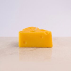 Vela decorativa artesanal hiperrealista en forma de porción de queso suizo amarillo con agujeros