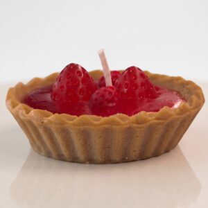 Vela artesanal hiperrealista en forma de tartaleta de fresa con bordes ondulados, relleno rojo y fresas